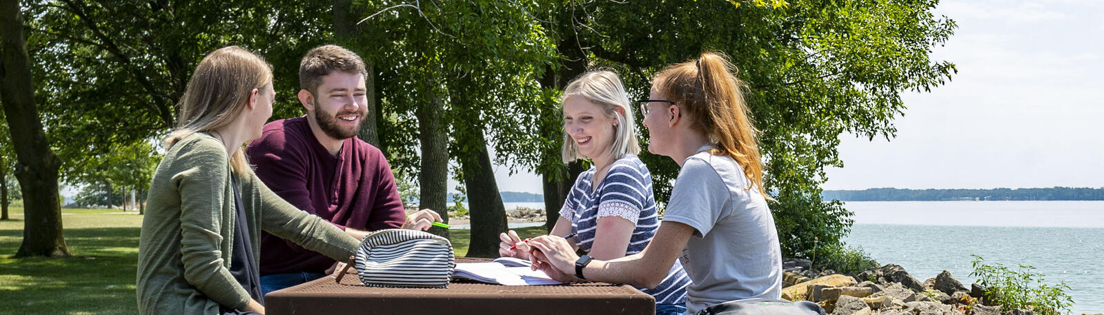 photo of students sitting at a picnic table by the lake on campus