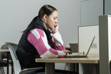 photo of a student sitting at a table looking at a laptop